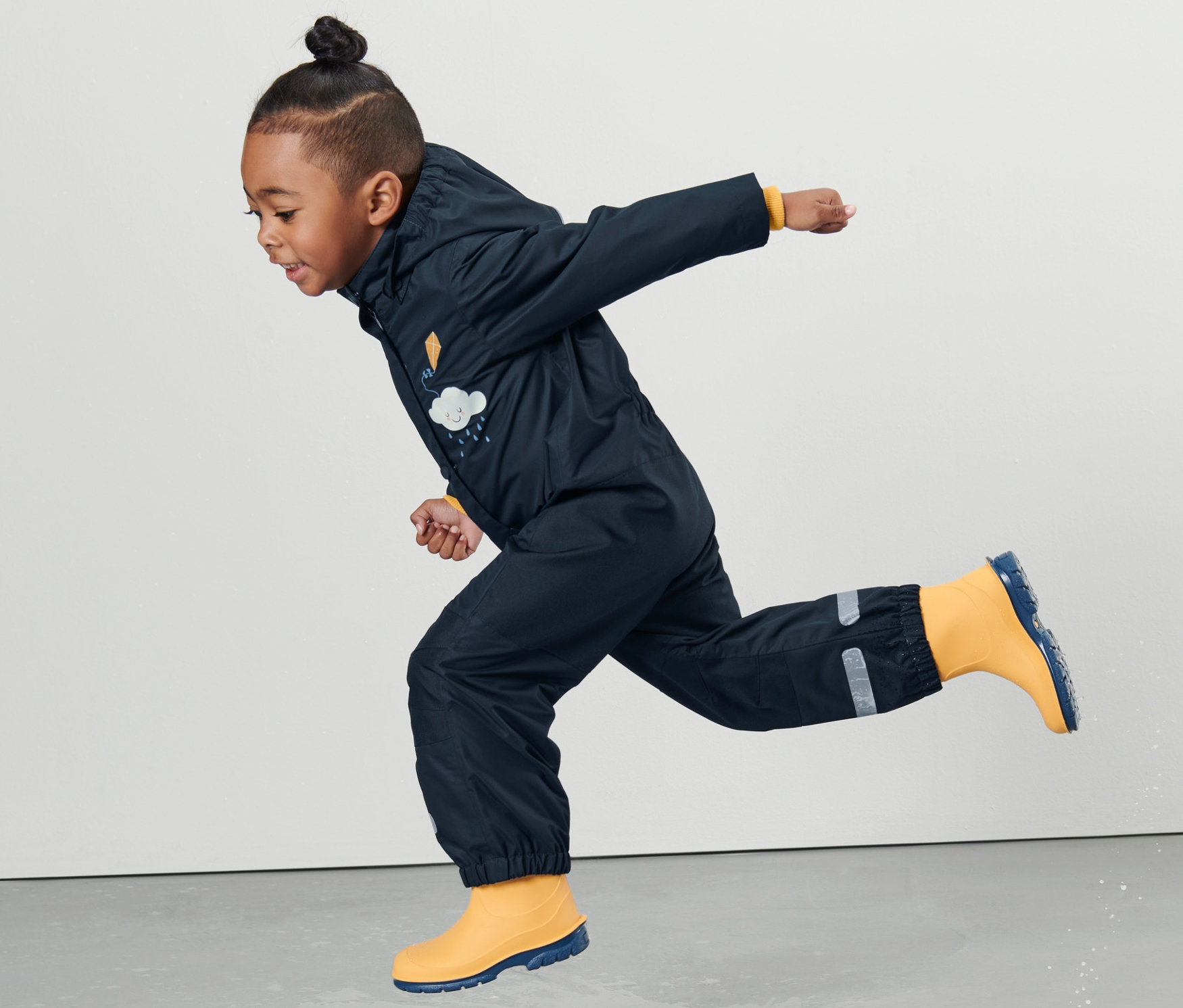 Un enfant en une-pièce imperméable pour tout-petit saute dans une flaque.