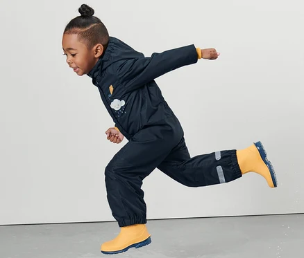 Un enfant en une-pièce imperméable pour tout-petit saute dans une flaque.