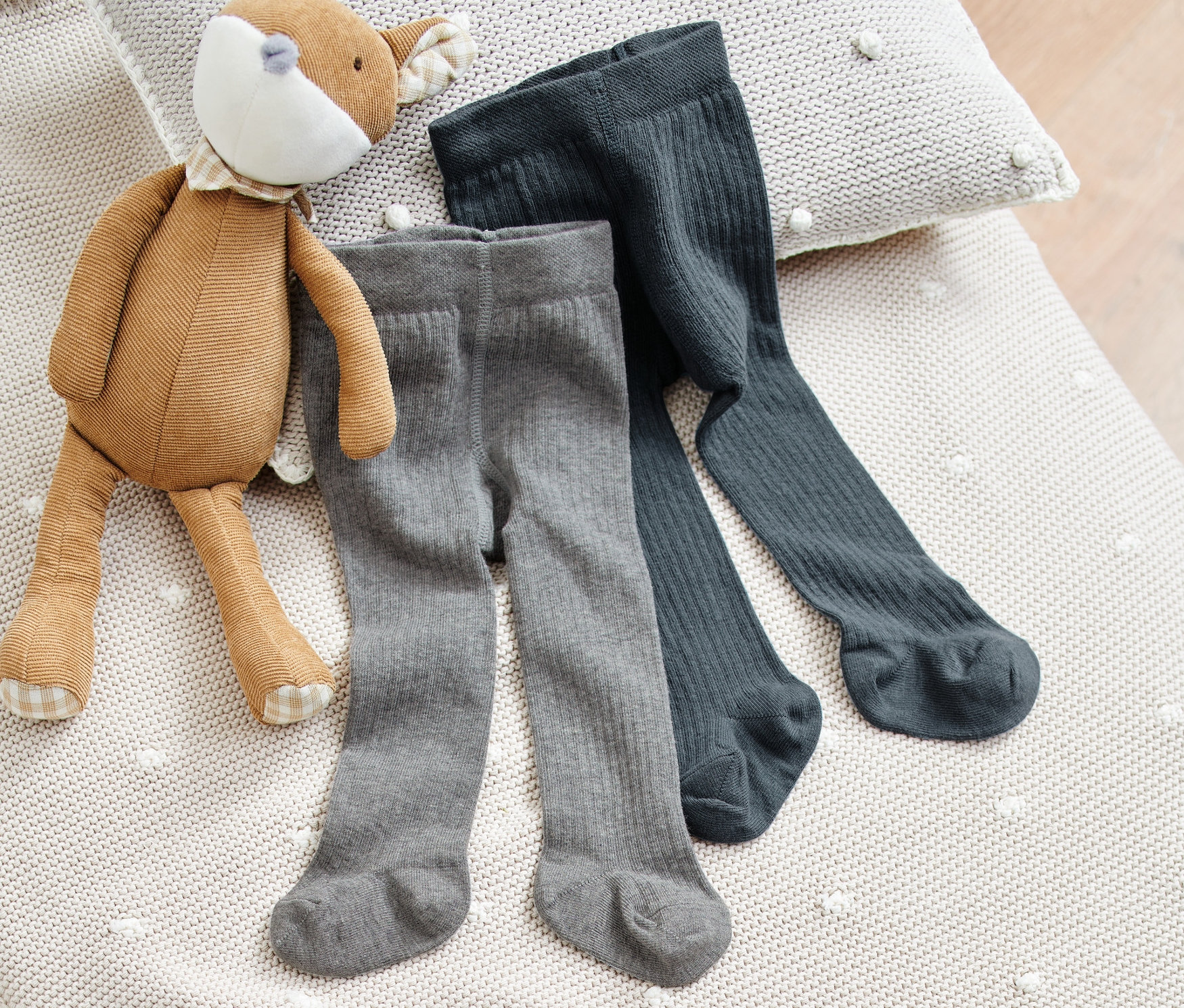 Deux paires de collants pour bébés sont posées sur une couverture en tricot à côté d'une peluche.