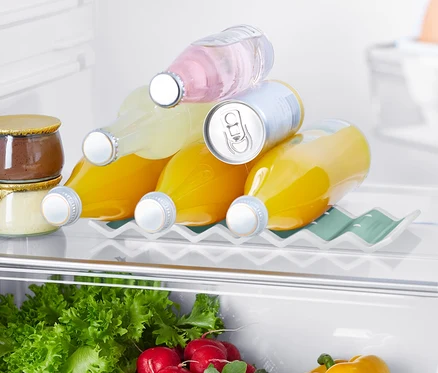 Dans le réfrigérateur, il y a un support de bouteille pour réfrigérateur sur lequel reposent trois bouteilles de jus et une canette. Dans la partie inférieure, on peut voir des salades, des radis et un poivron jaune.