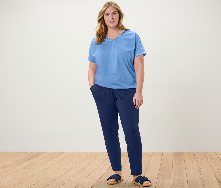 Une femme debout portant une blouse bleu clair avec un ruban au crochet et un pantalon en jersey bleu foncé.