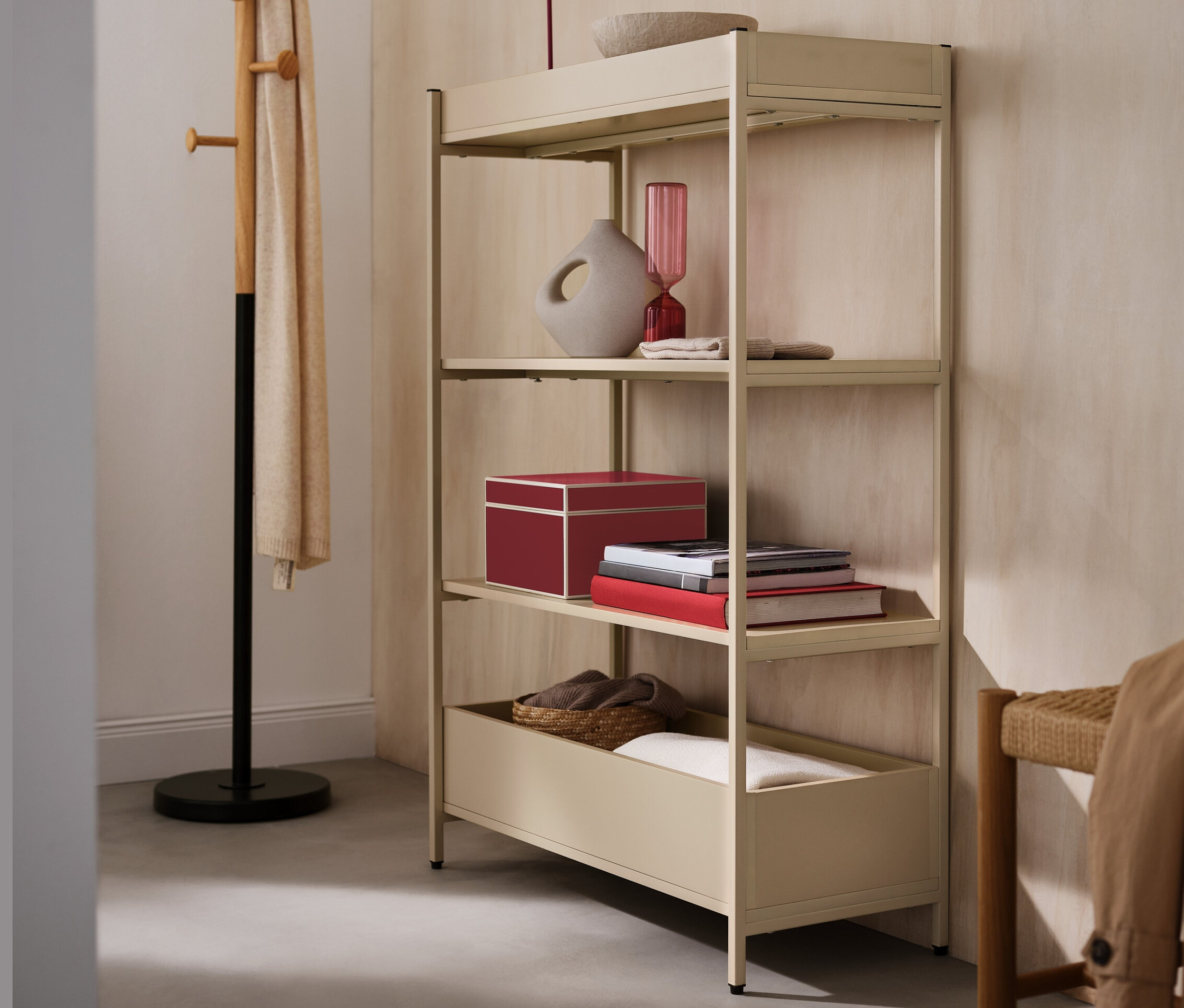 Console beige avec quatre étagères, sur laquelle se trouvent une lampe de table à LED rouge sans fil, un vase et un bol. À côté se trouve un porte-manteau.