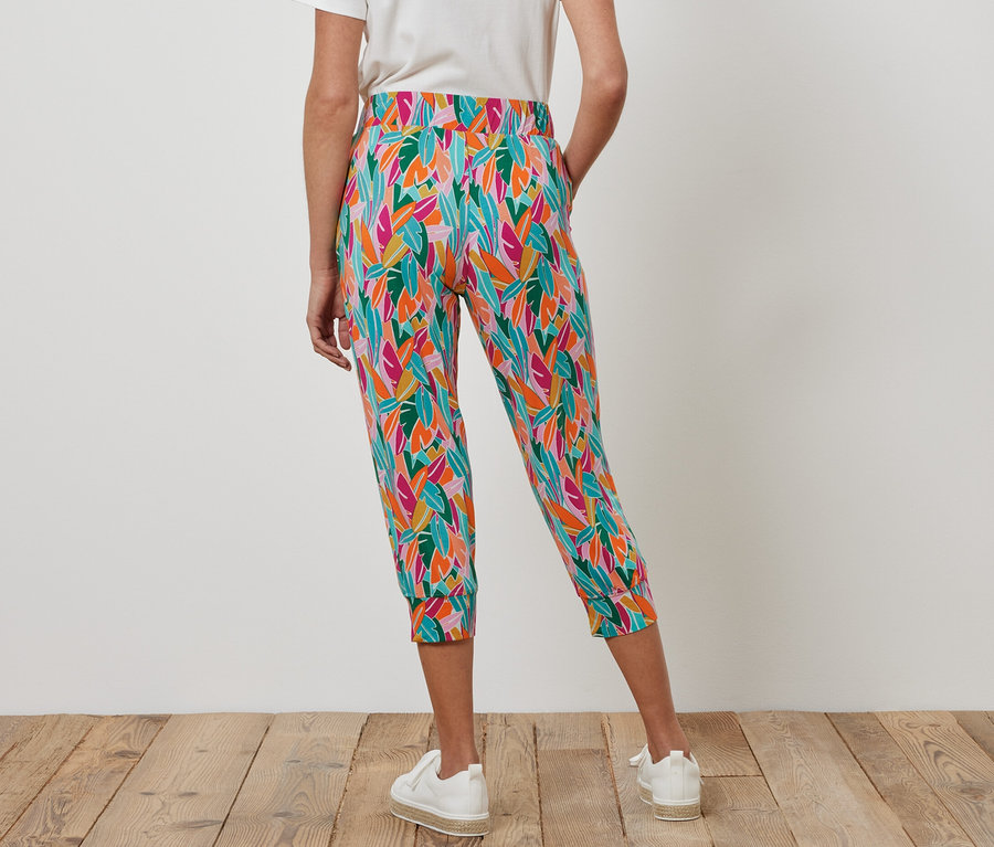 Une femme porte un pantalon 3/4 en jersey multicolore et des baskets blanches.