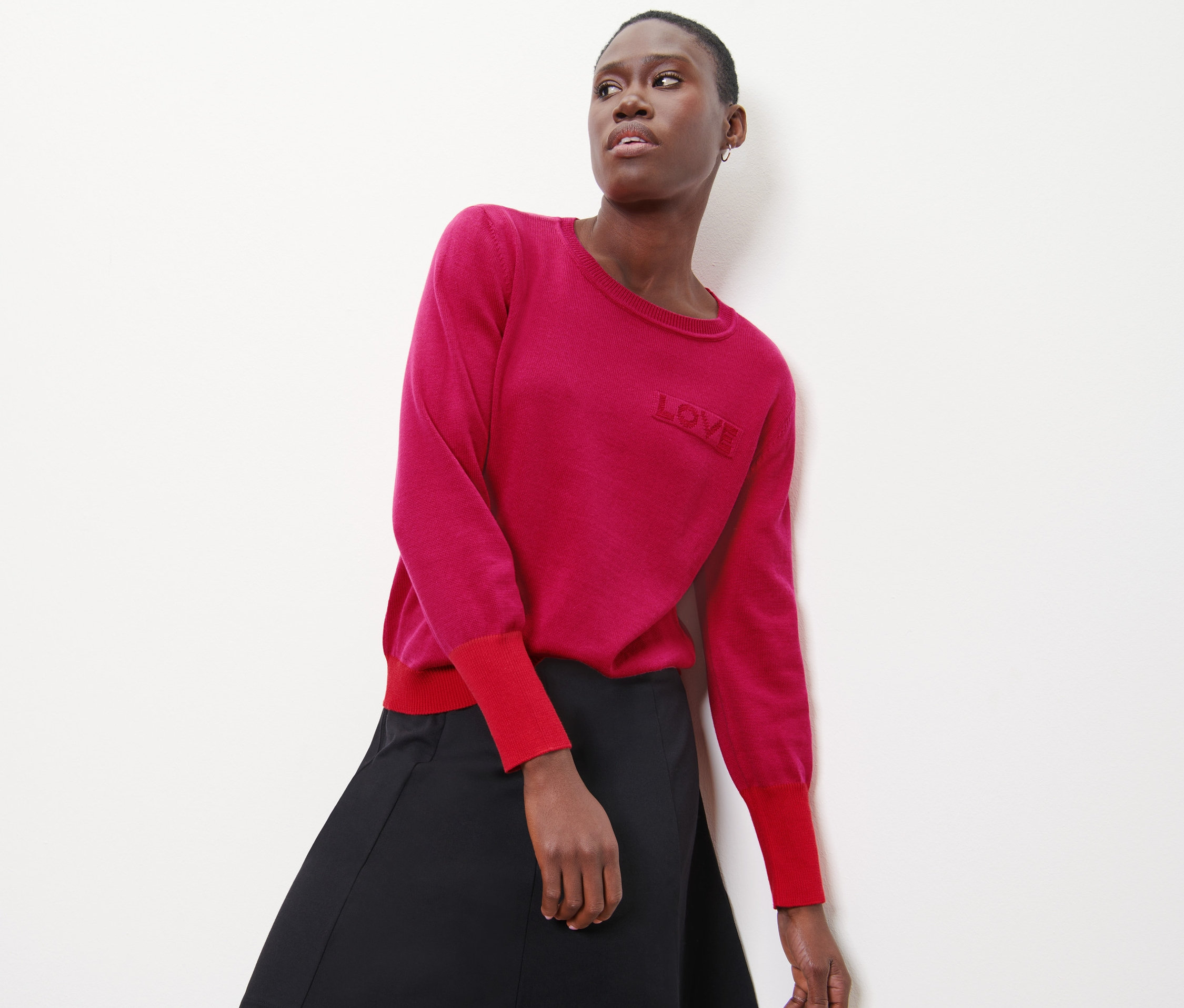 Femme posant dans un pull rose avec texte et une jupe noire.