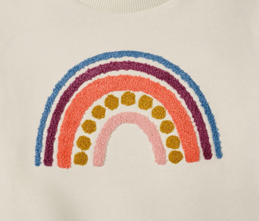 Détail d'un sweatshirt pour enfant avec motif arc-en-ciel appliqué.