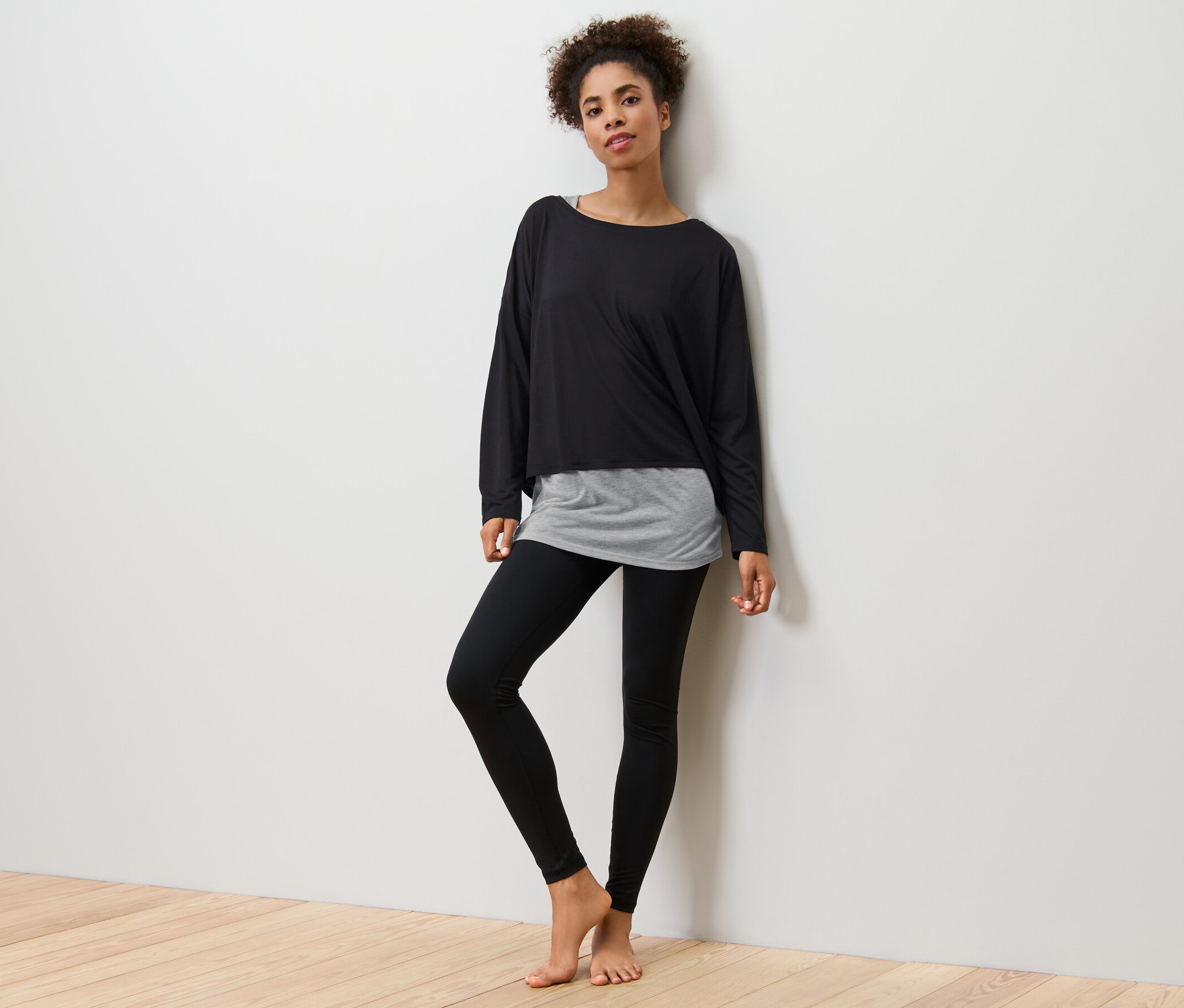 Femme posant en T-shirt de sport 2 en 1 noir et leggings noirs.
