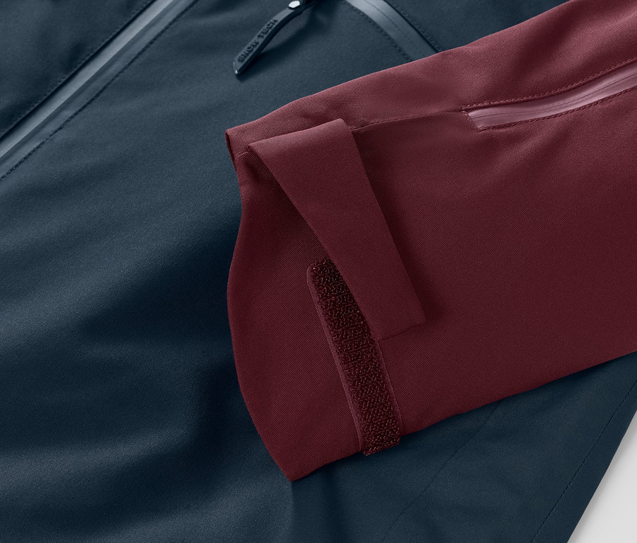 Gros plan sur une veste de ski et de snowboard : manche bordeaux avec manchette Velcro réglable et reste de la veste bleu marine.