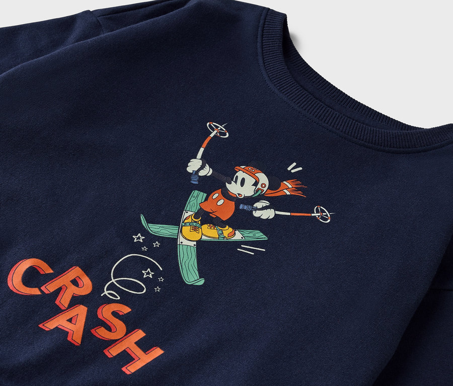 Sur un sweat-shirt bleu marine figure un dessin animé de Mickey Mouse faisant du ski.