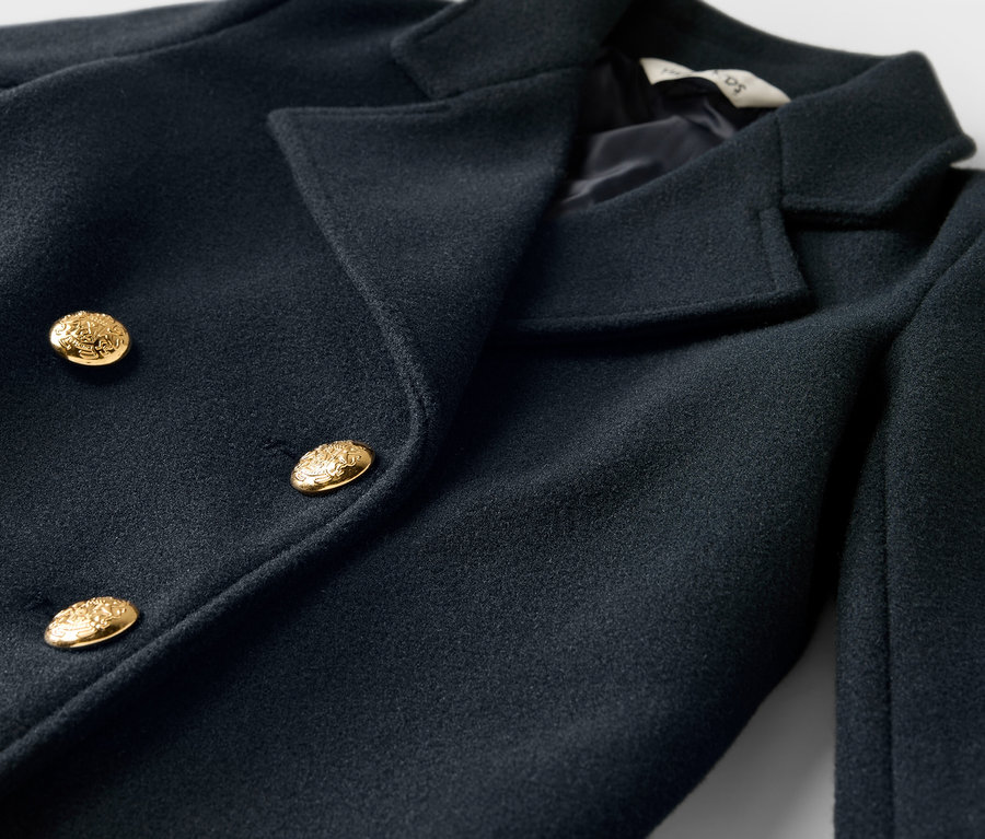 Gros plan sur un manteau croisé bleu foncé avec des boutons dorés.
