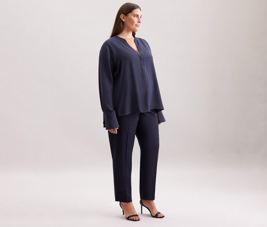 Femme debout de profil, portant une tunique en viscose Seidensticker bleu marine, un pantalon et des sandales.