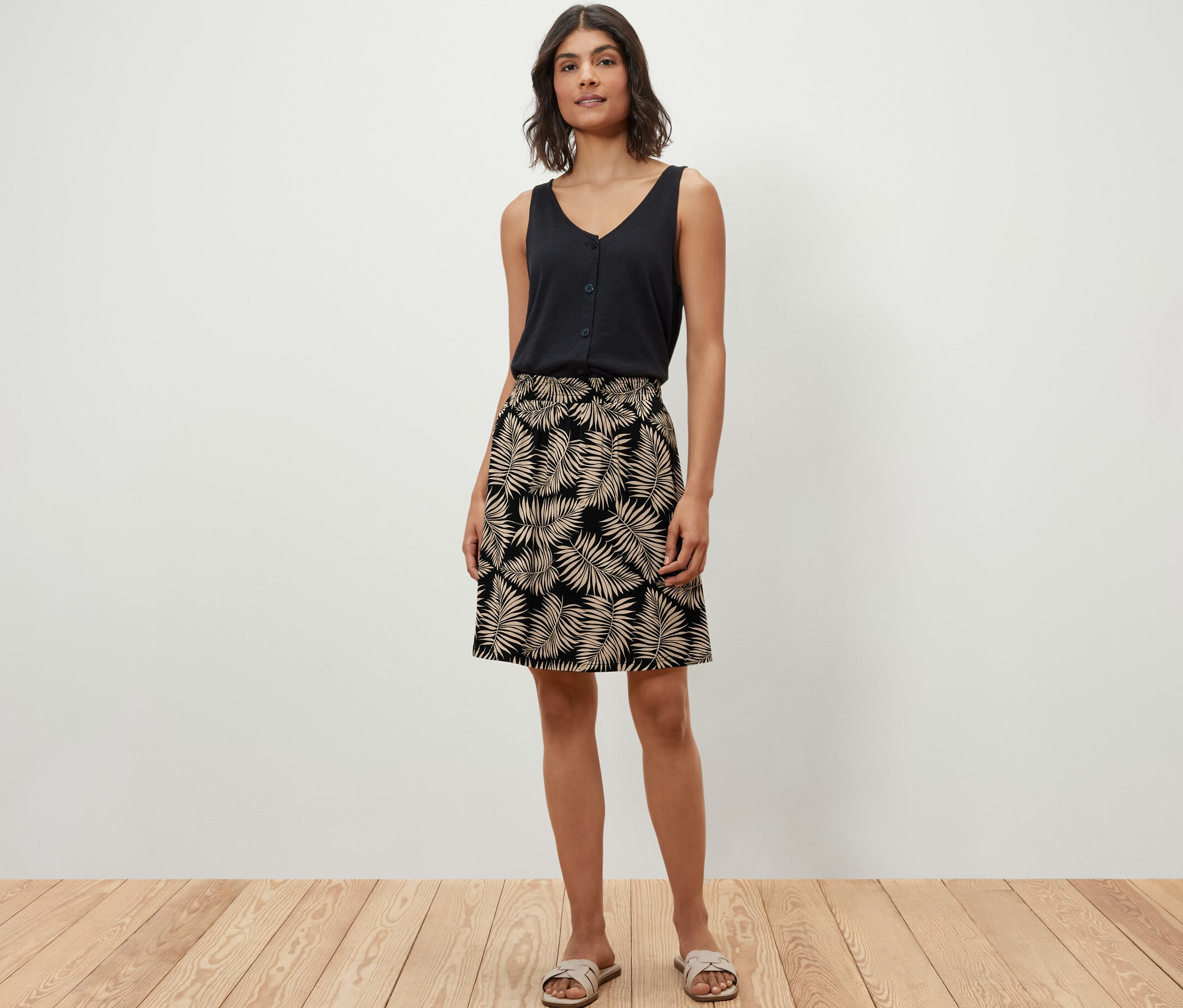 Une femme pose sur un plancher en bois, portant un haut noir et une robe en jersey imprimée.