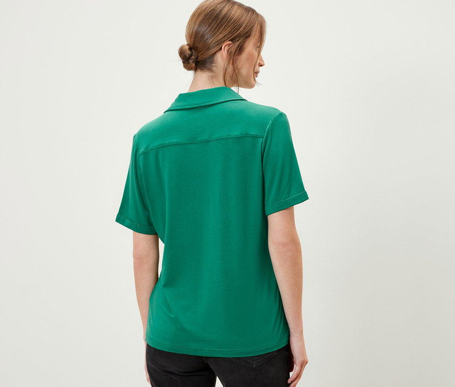 Vue arrière d'une femme portant une blouse avec patte de boutonnage émeraude et un short noir.