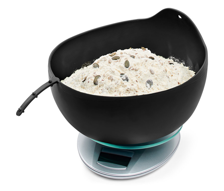 Un bol noir avec de la farine et des graines sur une balance digitale.