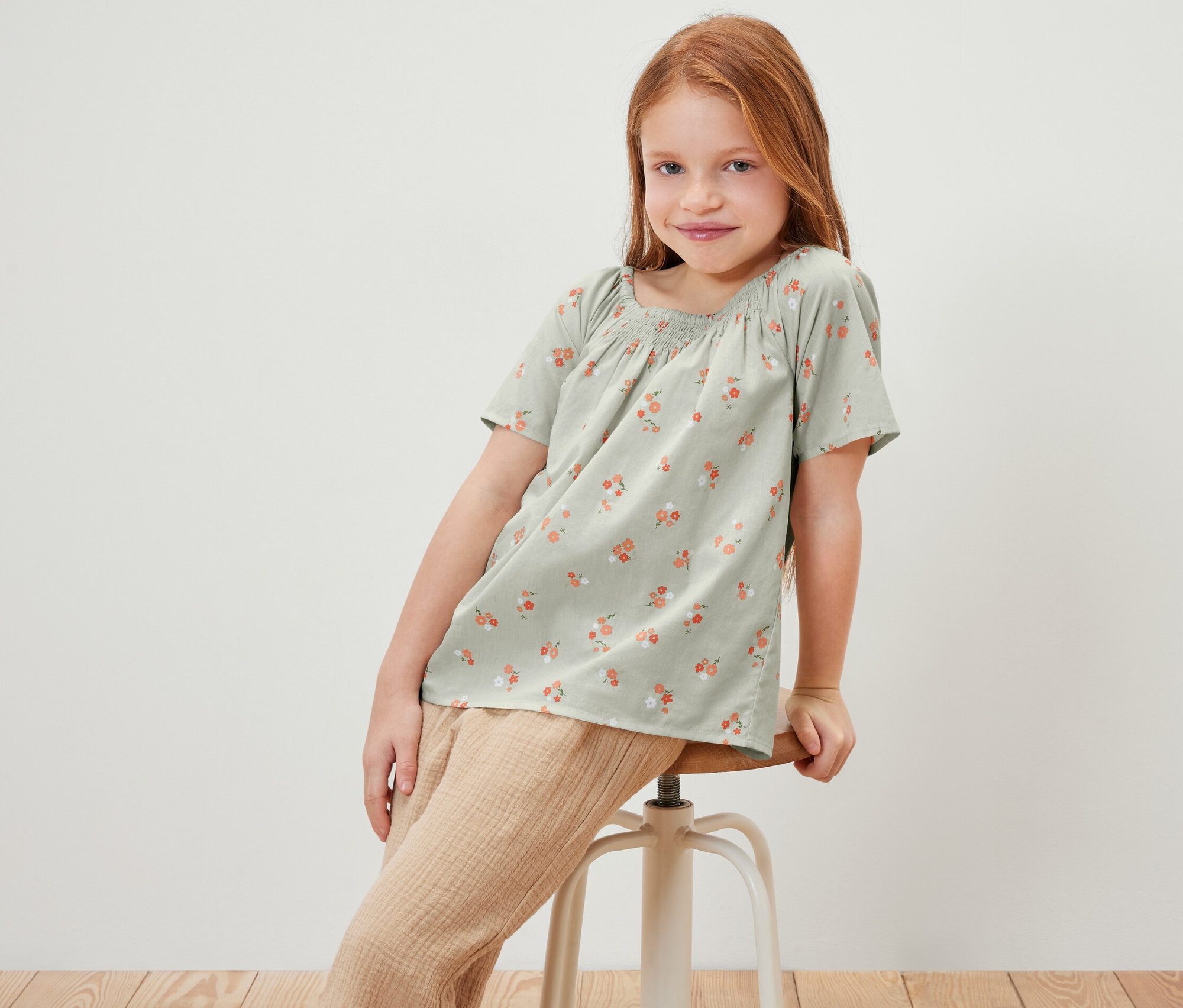 Fillette assise sur un tabouret portant une blouse pour enfant à motif floral.