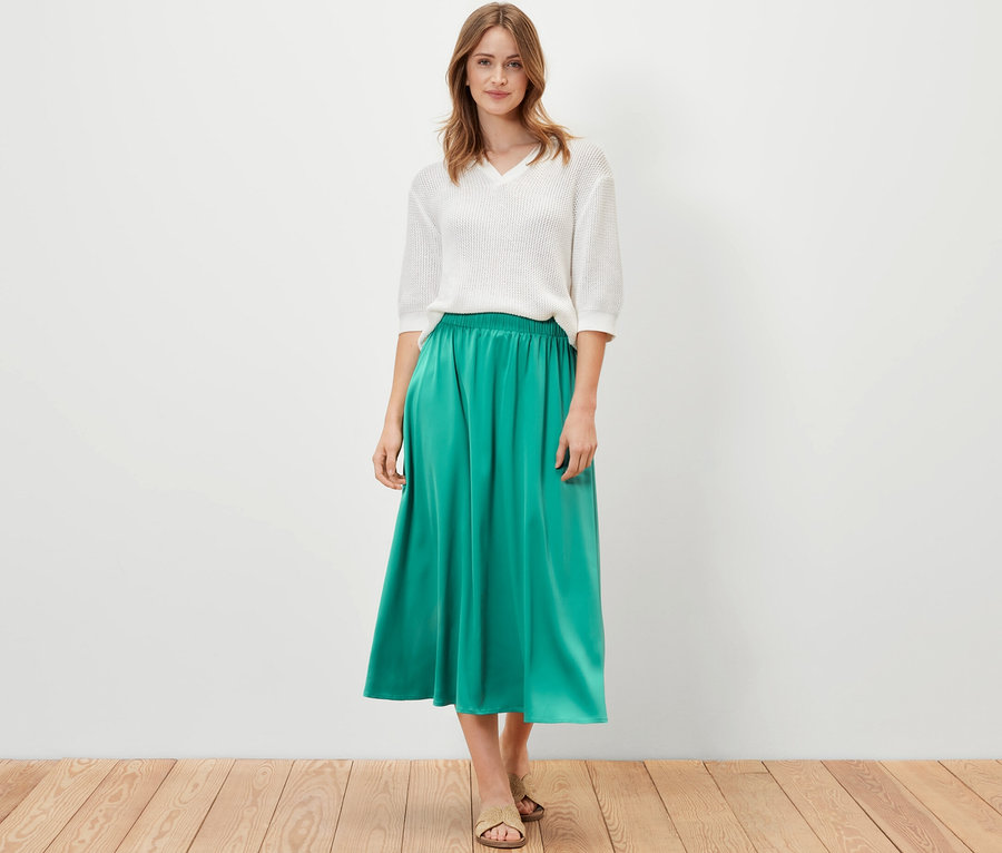 Femme posant dans un haut blanc et une jupe en satin verte.