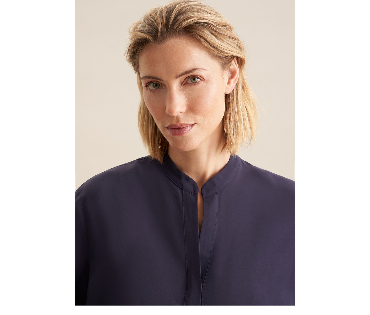 Femme blonde portant une tunique en viscose Seidensticker bleu marine avec col montant et encolure en V.