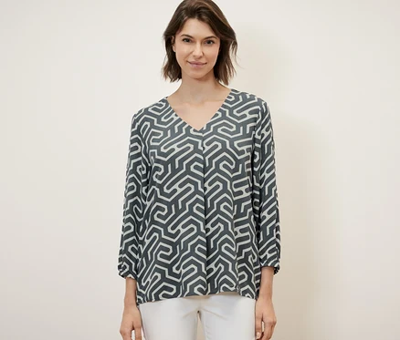 Une femme porte une blouse aspect froissé et un pantalon blanc.