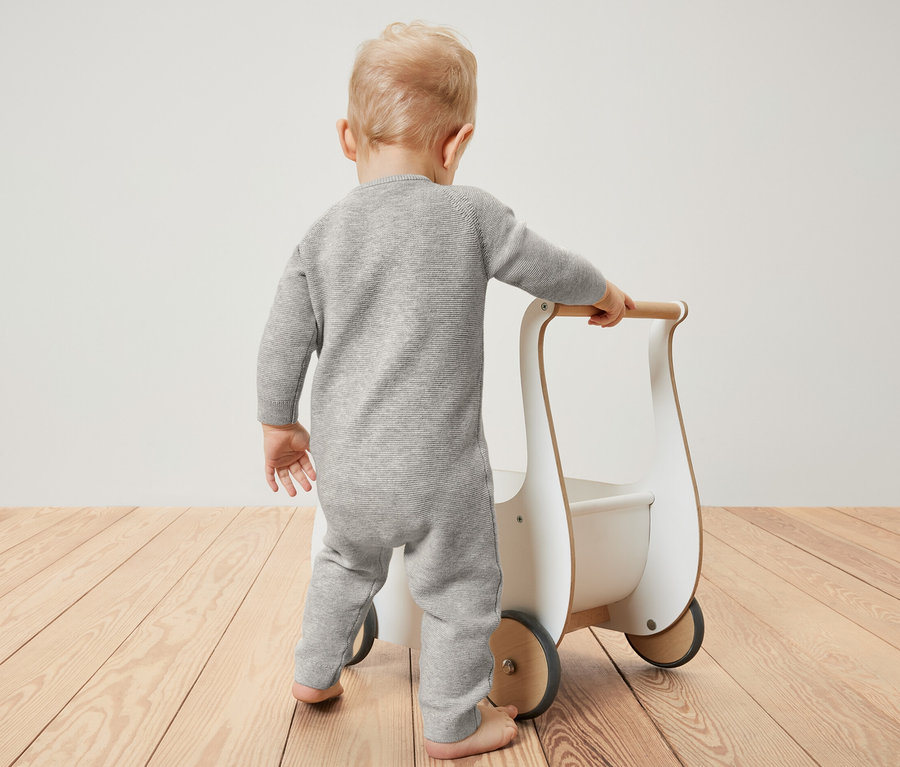 Bébé en combinaison en maille poussant un trotteur.