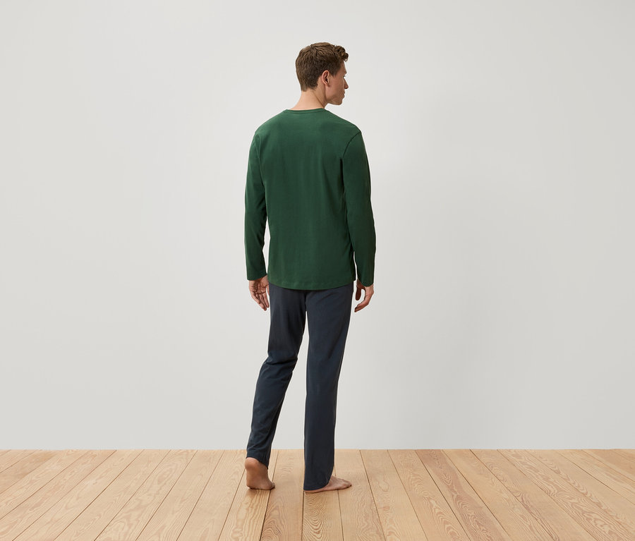 Un homme vu de dos porte un t-shirt vert à manches longues et un pantalon bleu marine.