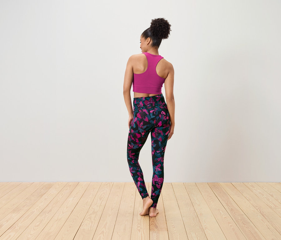 Une femme, dos à la caméra, porte un soutien-gorge de sport rose et un legging noir avec un motif floral rose et bleu.