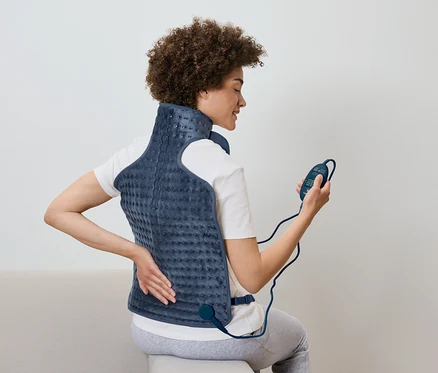 Une femme est assise et utilise un coussin chauffant dorsal avec une télécommande à la main.