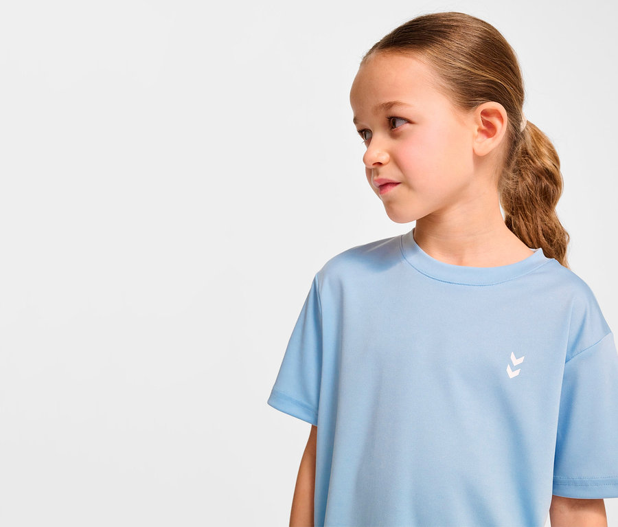 Fillette portant un t-shirt d'entraînement HUMMEL HMLJR pulse bleu clair regardant vers la droite.
