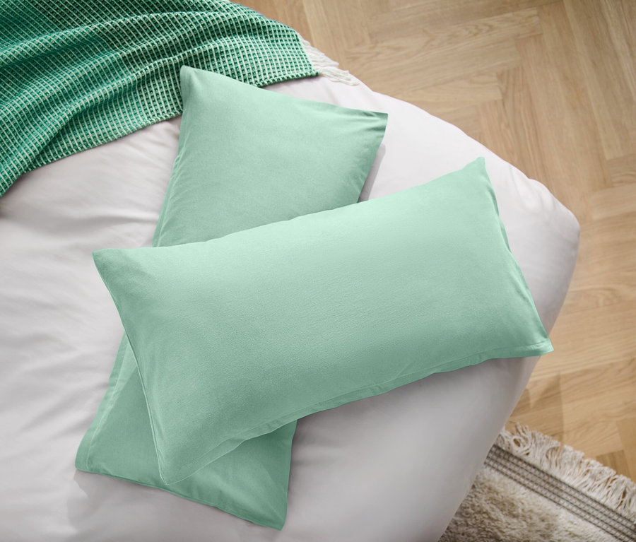Deux oreillers vert clair sur un drap blanc à côté d'une couverture verte.