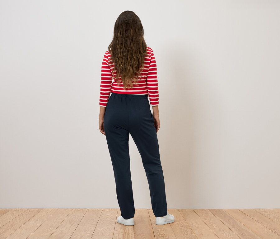Femme portant un haut rayé rouge et blanc et un pantalon bleu marine, dos à la caméra.