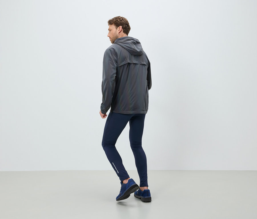 Un homme portant une veste à capuche grise, des leggings bleu marine et des baskets se tient dos au spectateur.