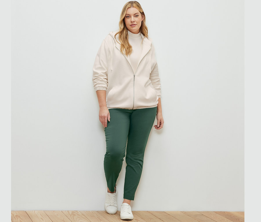 Femme posant et portant une jaquette en sweat blanc crème, un pantalon stretch et une blouse à col montant.