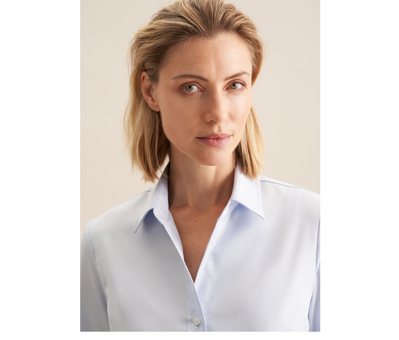 Femme aux cheveux blonds portant un chemisier en tulle Seidensticker bleu clair, regardant devant elle.