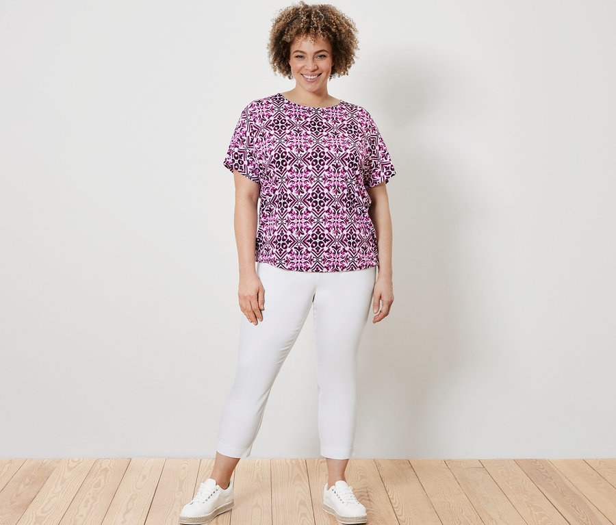 Femme posant dans un chemisier imprimé, baies, et un pantalon stretch 7/8, blanc.