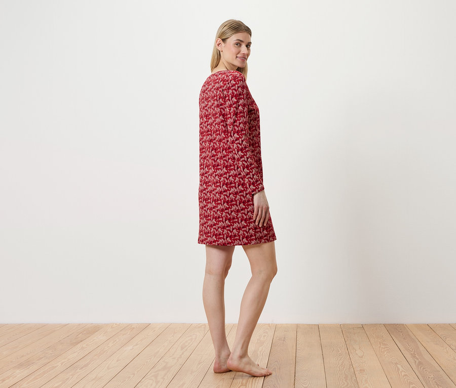 Une femme se tient de côté et porte une robe rouge à motifs.