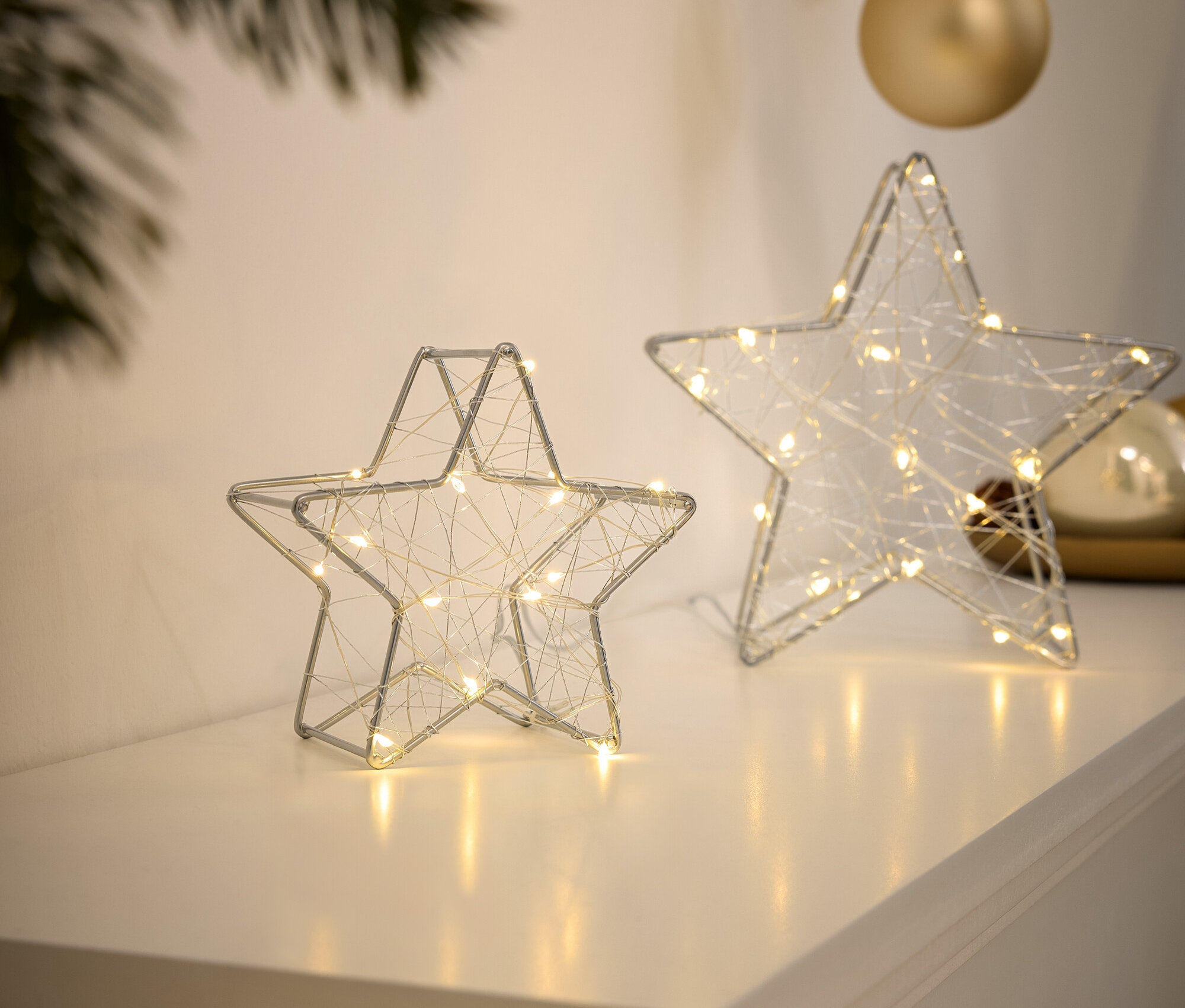 Deux étoiles en fil de fer argentées avec de petites lumières sont posées sur une surface blanche.