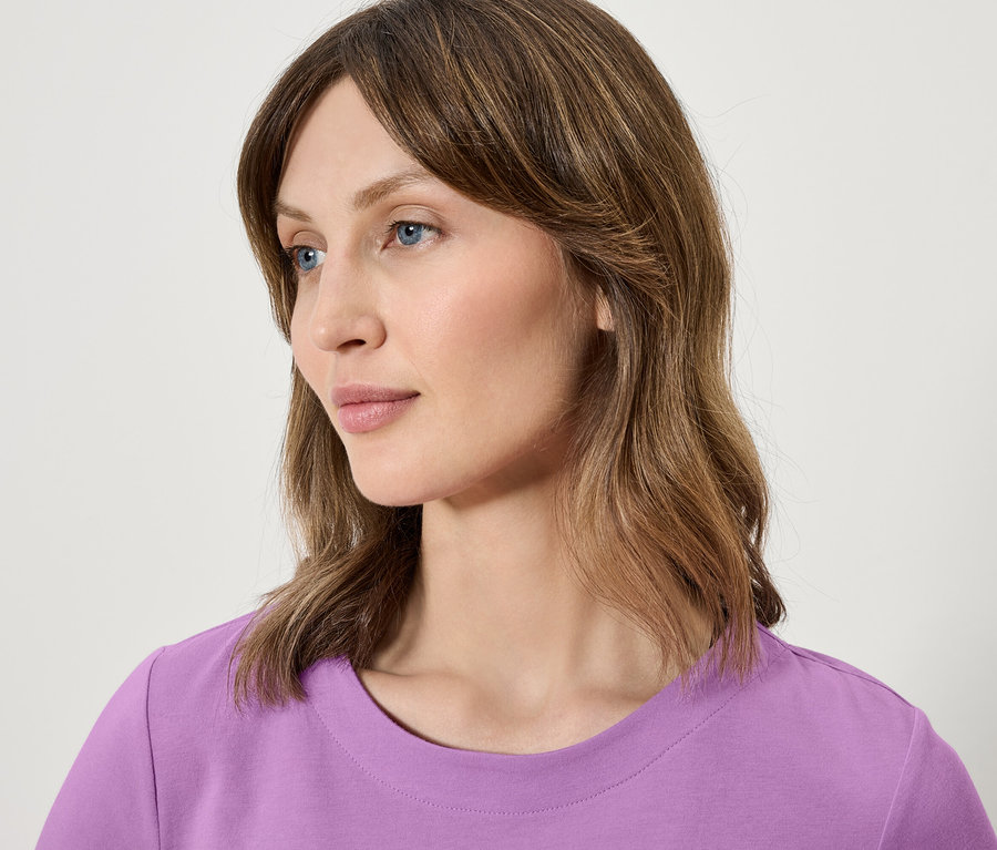 Gros plan portrait d'une femme aux cheveux bruns et aux yeux bleus portant un t-shirt violet.
