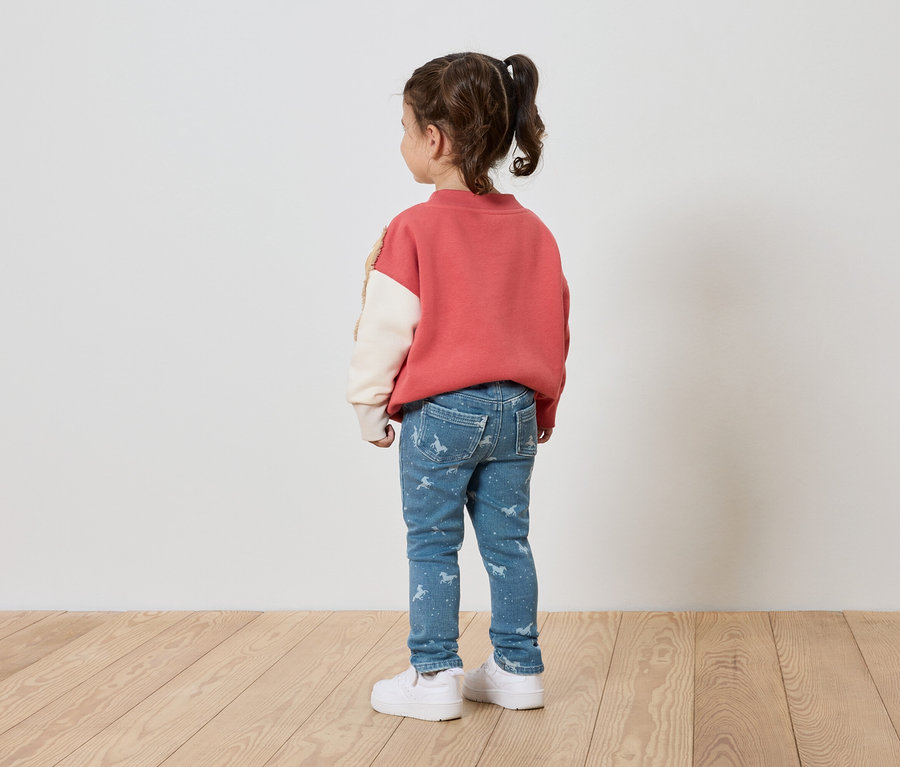 Une fille portant un sweat-shirt rose, un jean bleu imprimé et des chaussures blanches, est dos à l'appareil photo.