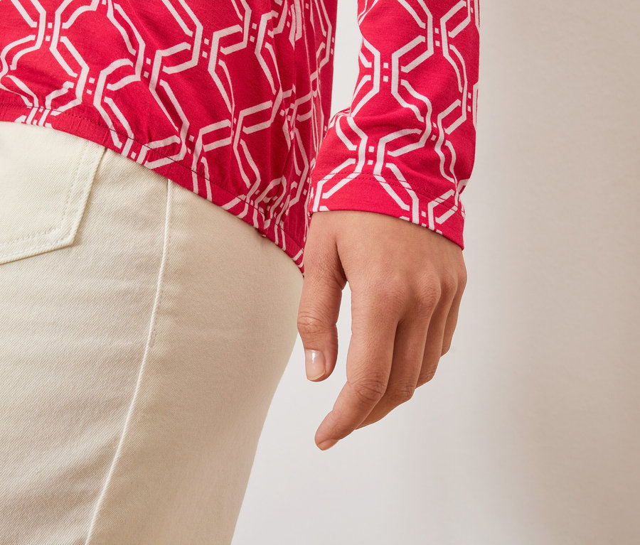 Gros plan sur la main d'une femme, un haut rouge et blanc et un pantalon clair.