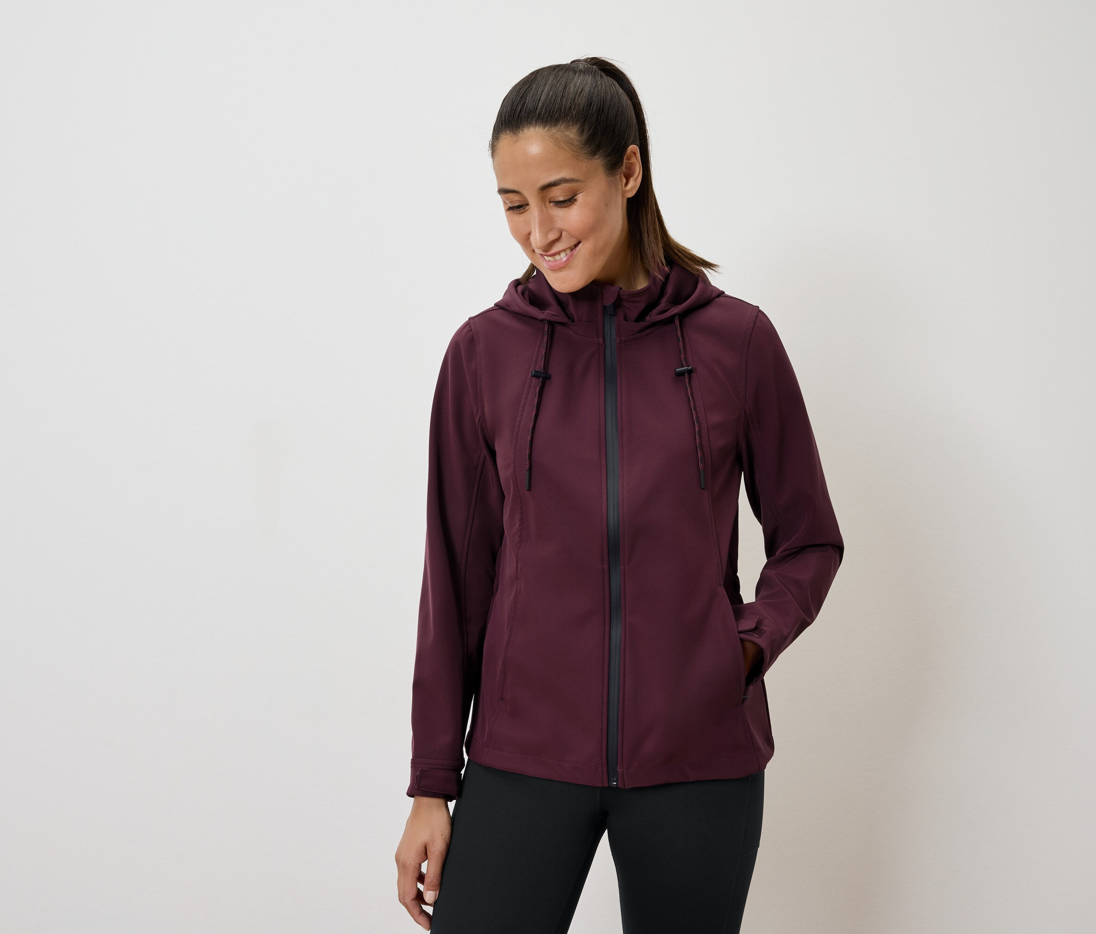 Femme portant une veste à capuche bordeaux et un legging noir.