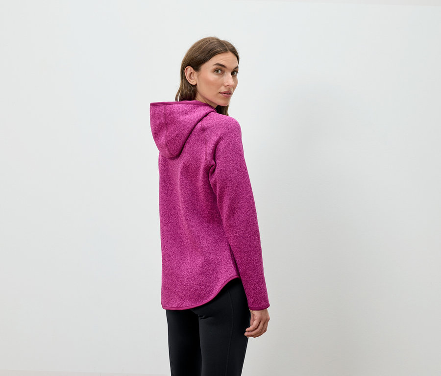 Une femme regarde par-dessus son épaule et porte un sweat à capuche rose et un pantalon noir.