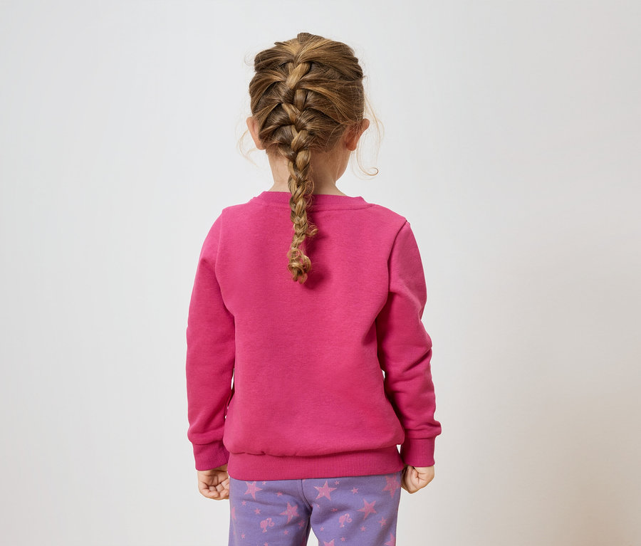 Une fillette avec une tresse, vue de dos, porte un sweat-shirt rose et un pantalon violet avec des étoiles.