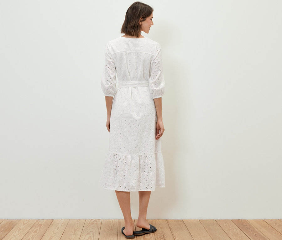 Une femme se tient dos à la caméra et porte une robe avec broderie ajourée.