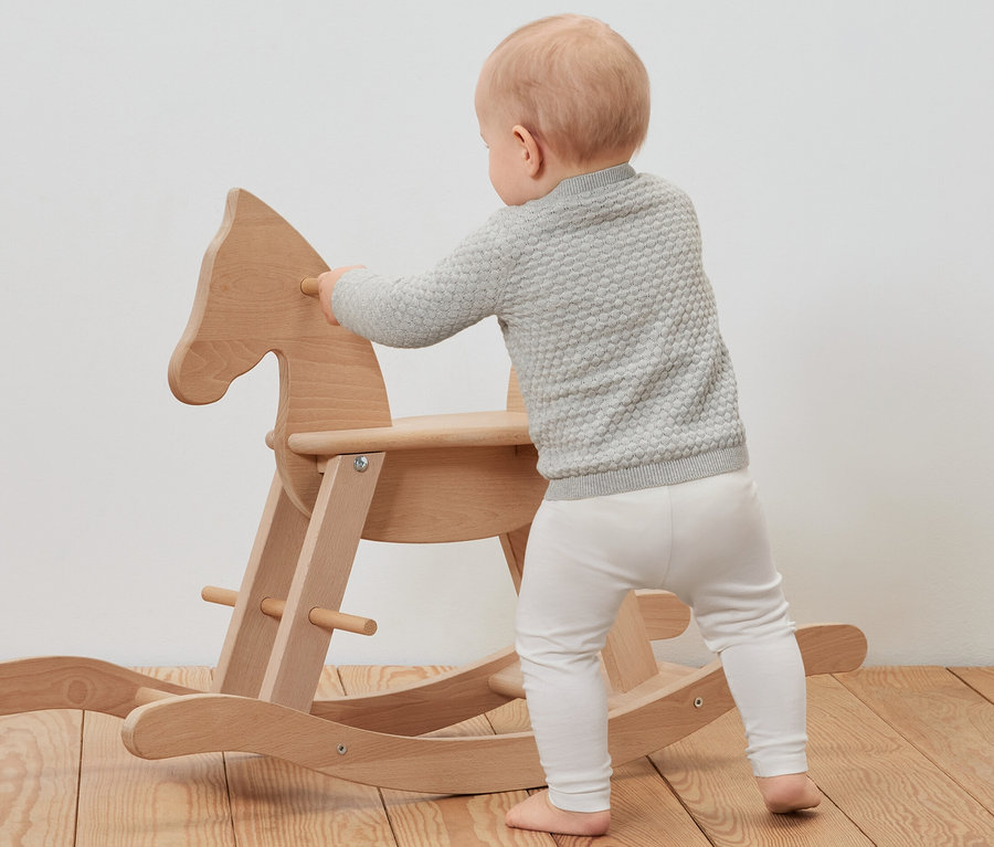 Un bébé portant une veste en maille s'appuie sur un cheval à bascule en bois.