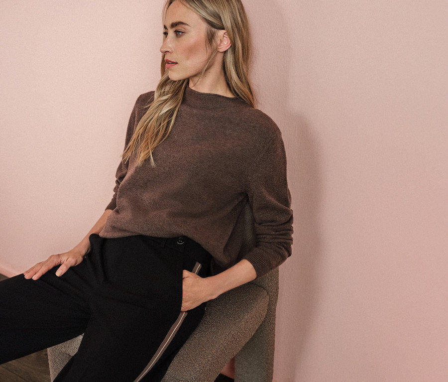 Femme assise sur une chaise portant un pull marron et un pantalon noir Straight Leg avec galon de Street One.