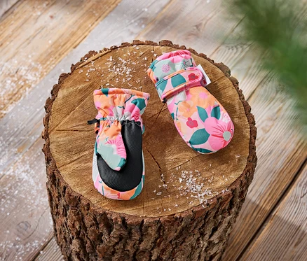 Des moufles pour enfants à motifs floraux sont posées sur une bûche de bois.