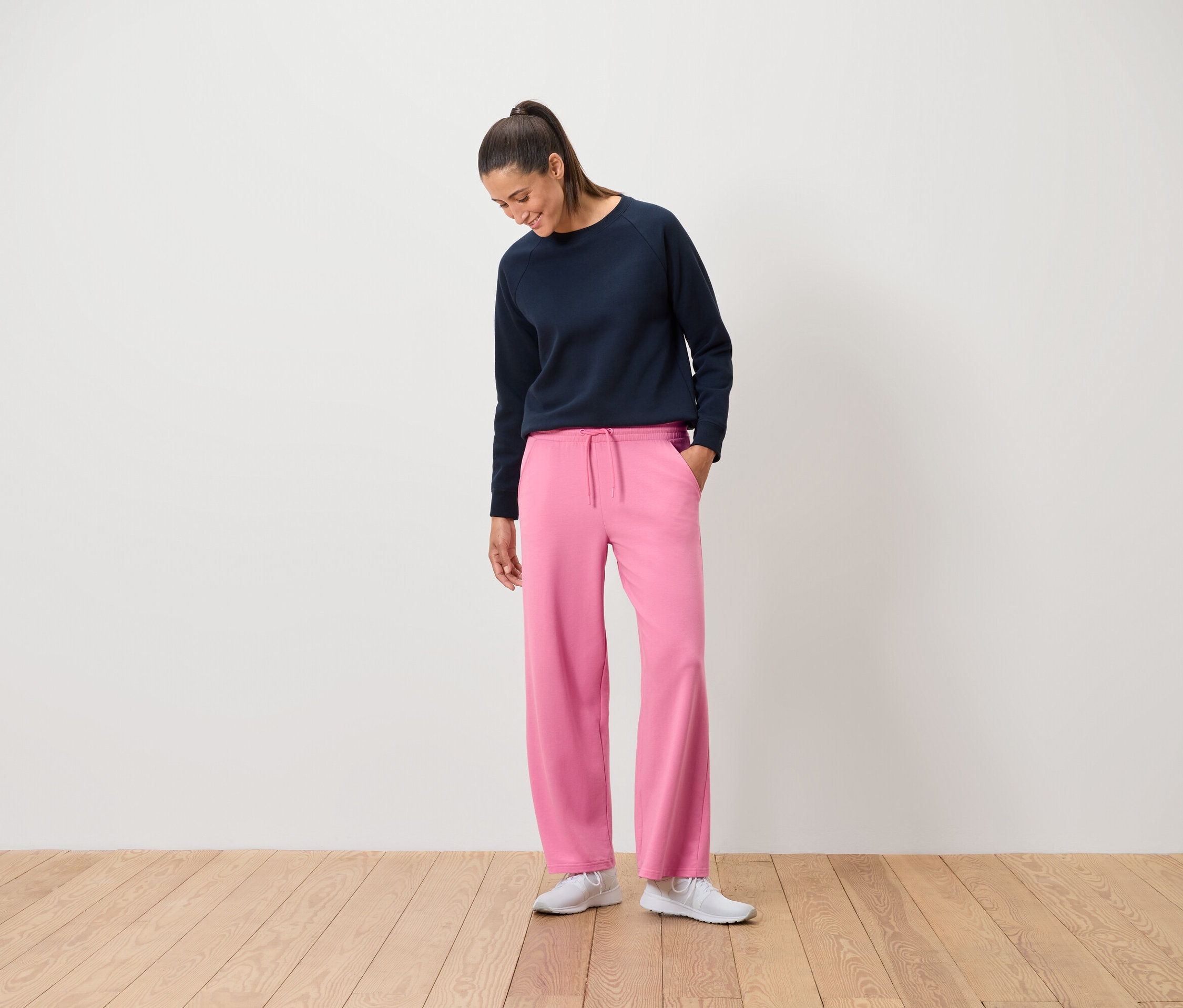 Une femme portant un sweat-shirt bleu marine et un pantalon rose se tient sur un plancher en bois.