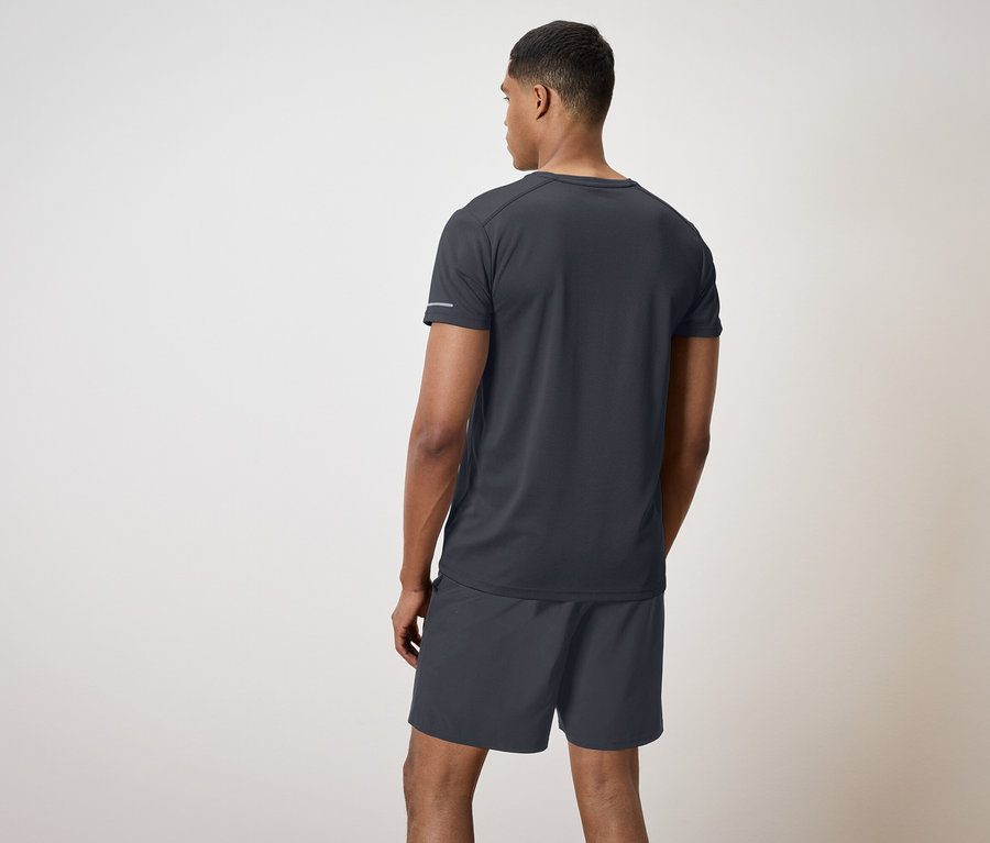 Un homme en t-shirt noir et short dos à la caméra.