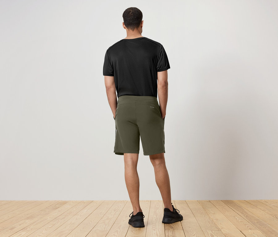 Un homme vu de dos porte un t-shirt noir et un short vert.