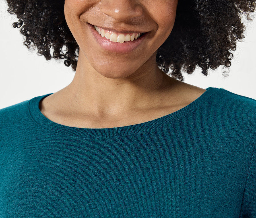 Gros plan d'une femme souriante avec une coiffure afro dans un pull bleu-vert.