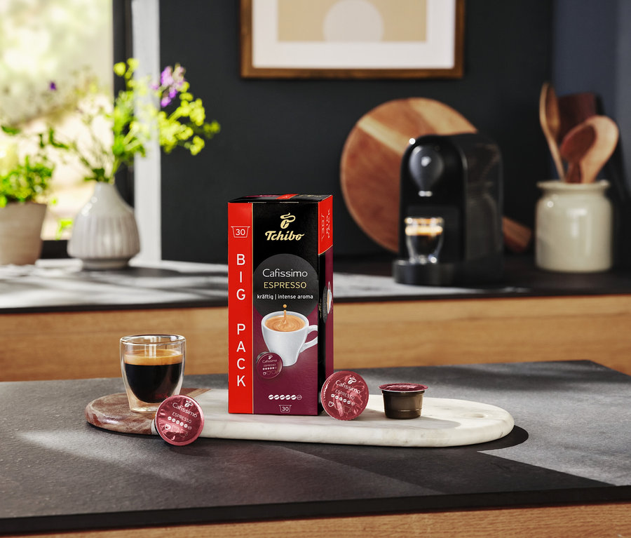 Un verre à expresso est posé à côté d'un paquet de Cafissimo Espresso kräftig et de capsules sur un plateau en marbre.