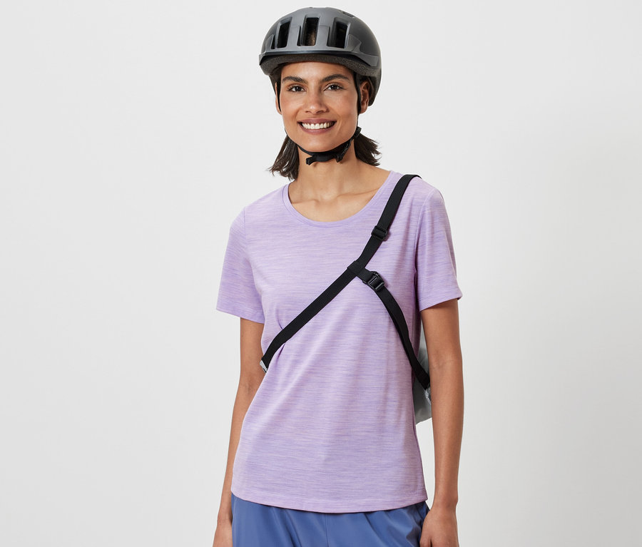 Femme souriante portant un casque de vélo avec des sacs à provisions pour vélo en bandoulière.